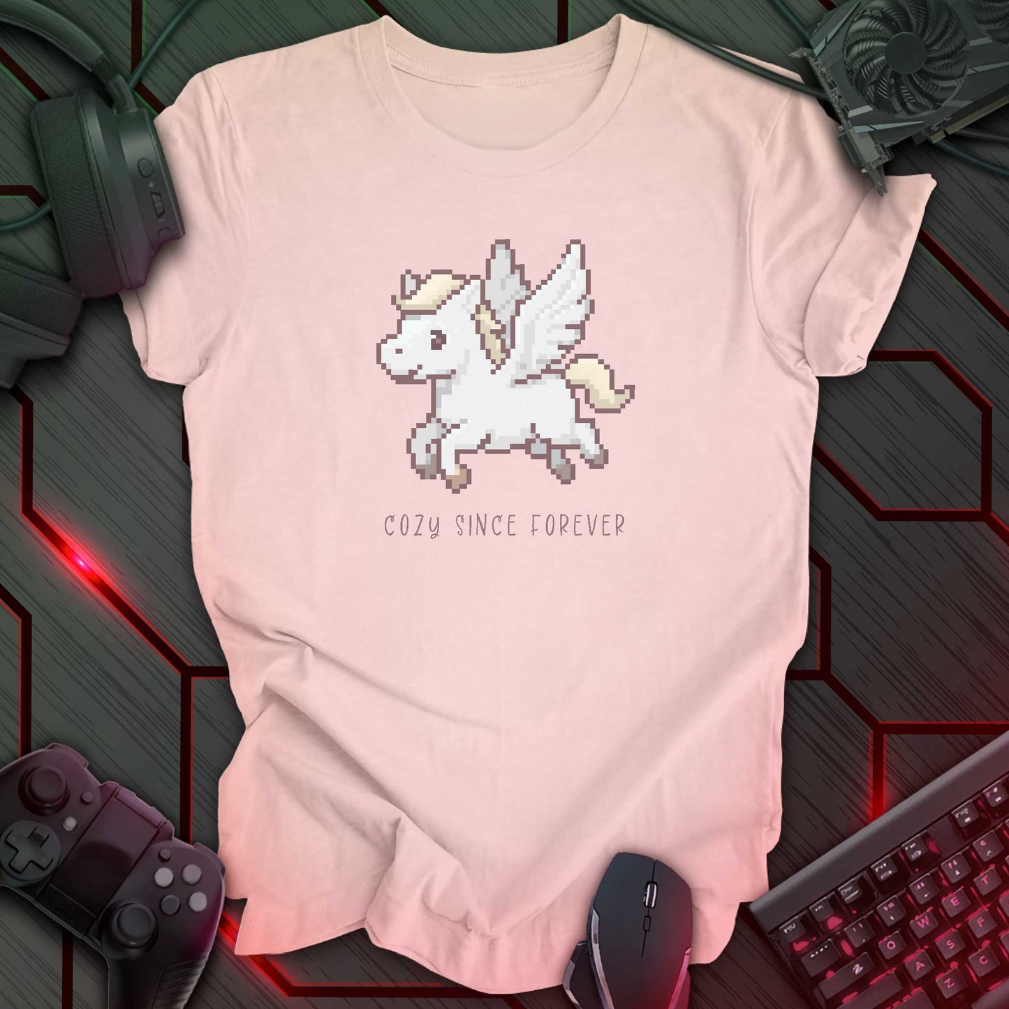 soft pink color t-shirt with a chest print of a pixel art cute winged Pegasus flying about handwritten styled text that reads "COZY SINCE FOREVER".