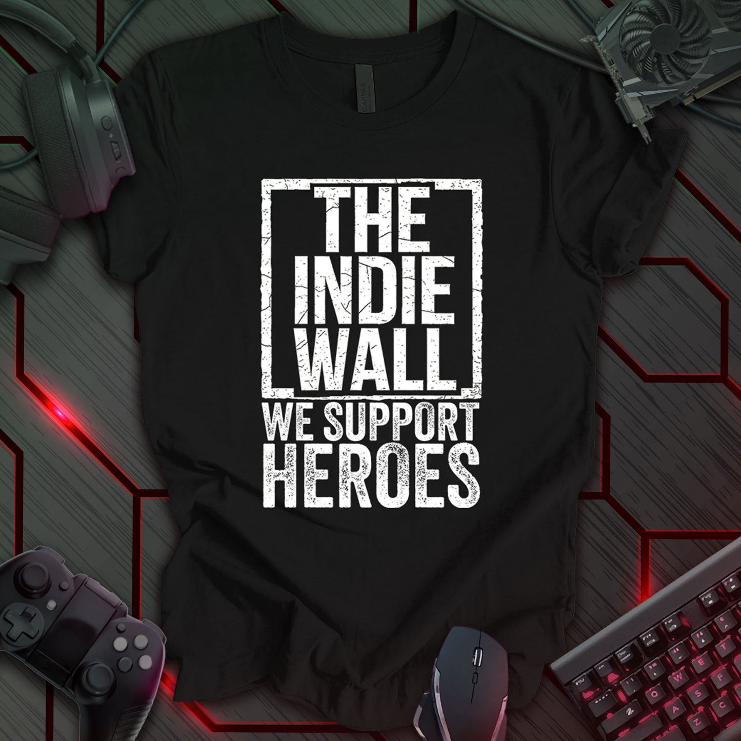 Black gaming t-shirt featuring a distressed black and white design of The Indie Wall logo. Below the logo, bold distressed text reads "WE SUPPORT HEROES," emphasizing support for indie developers and gamers.