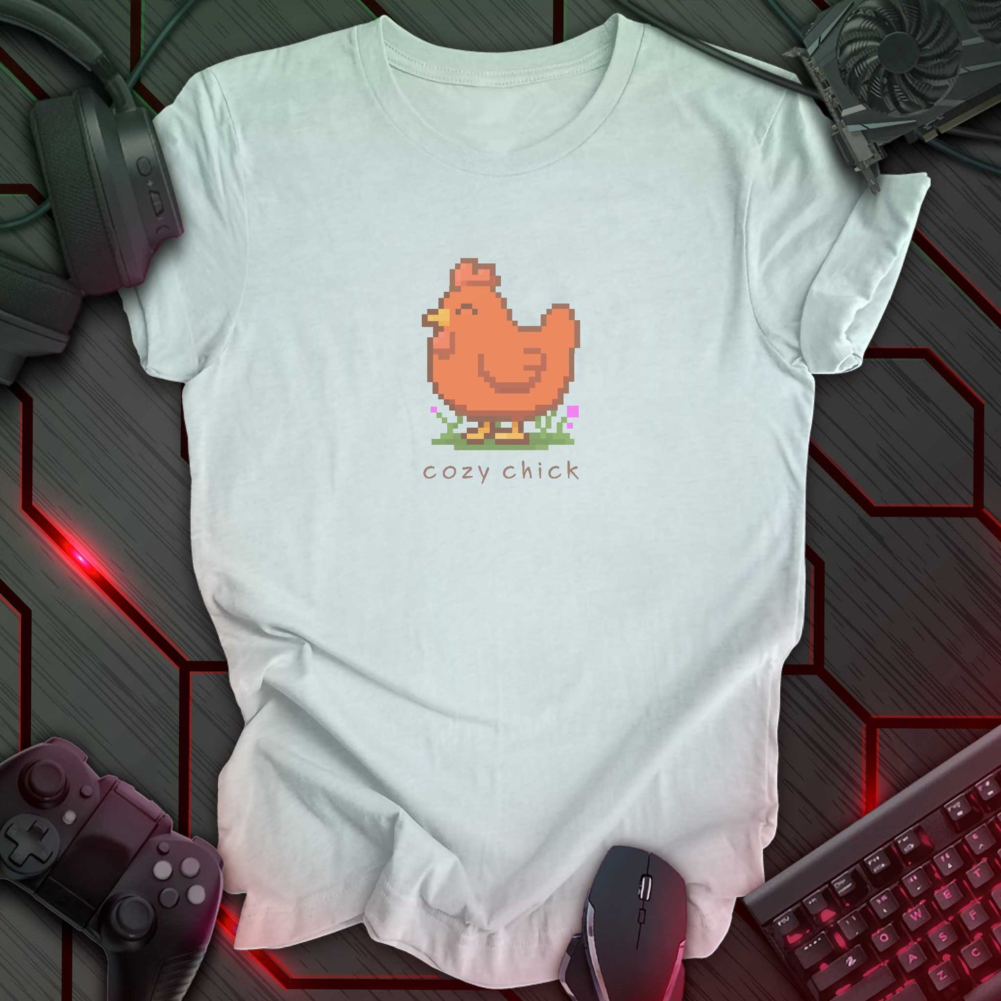 light blue t-shirt with a chest print of a pixel art image of a cute brown chick standing on a patch of grass. text beneath the pixel art reads "cozy chick".