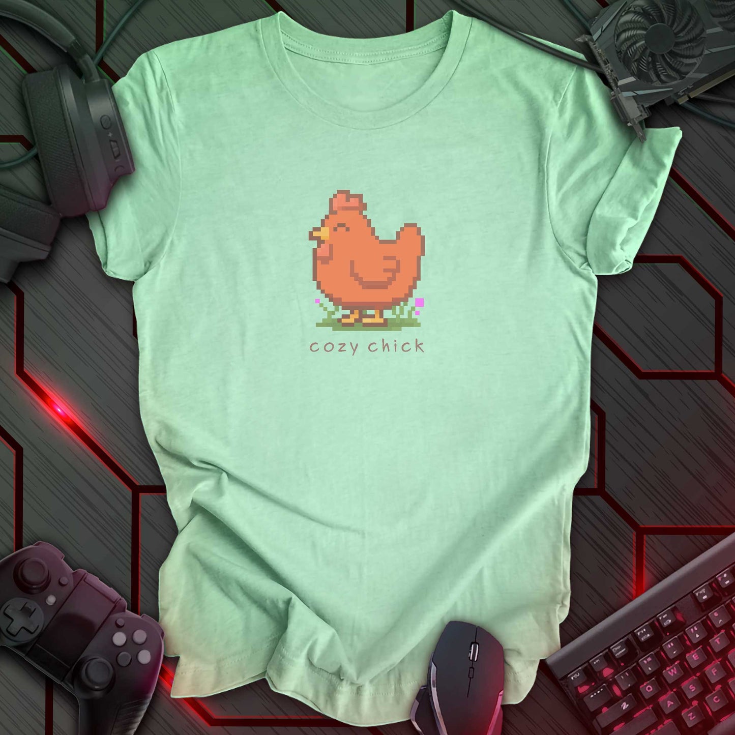light green color t-shirt with a chest print of a pixel art image of a cute brown chick standing on a patch of grass. text beneath the pixel art reads "cozy chick".