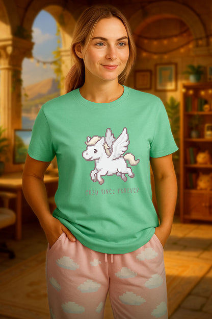 young woman wearing a mint green t-shirt with a chest print of a pixel art cute winged Pegasus flying about handwritten styled  text that reads "COZY SINCE FOREVER". she is standing in an ancient Greece themed cozy room. 