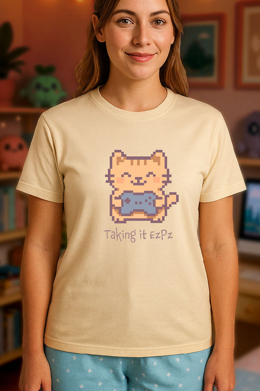 Pixel art cat holding a game controller with closed eyes, smiling above the phrase "Taking it EzPz" in kawaii cozy gamer style. Soft Cream color t-shirt