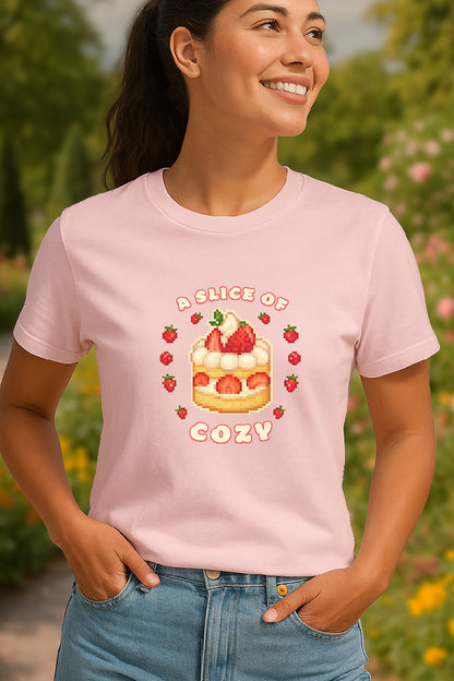 Young woman standing in a summer garden wearing a soft pink colored t-shirt with a pixel art strawberry shortcake surrounded by strawberries with text “A Slice of Cozy” in cute cozy gaming style.