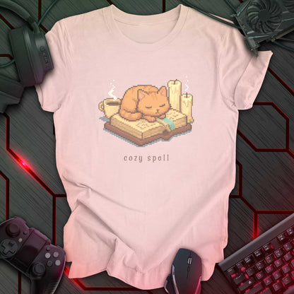 Pixel art orange cat sleeping on a book with candles and a coffee mug, under the text "cozy spell" in soft cozy gamer style. Soft Pink background.