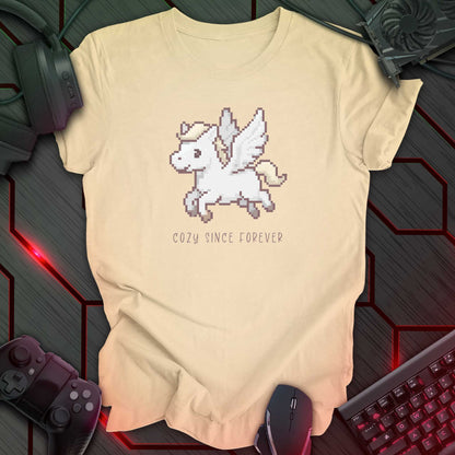 soft cream color t-shirt with a chest print of a pixel art cute winged Pegasus flying about handwritten styled  text that reads "COZY SINCE FOREVER". 