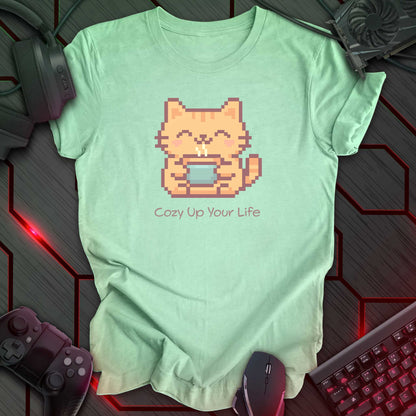 Pixel art orange cat holding a cup of hot tea with a happy expression on the cat's face. Print on a mint green t-shirt.