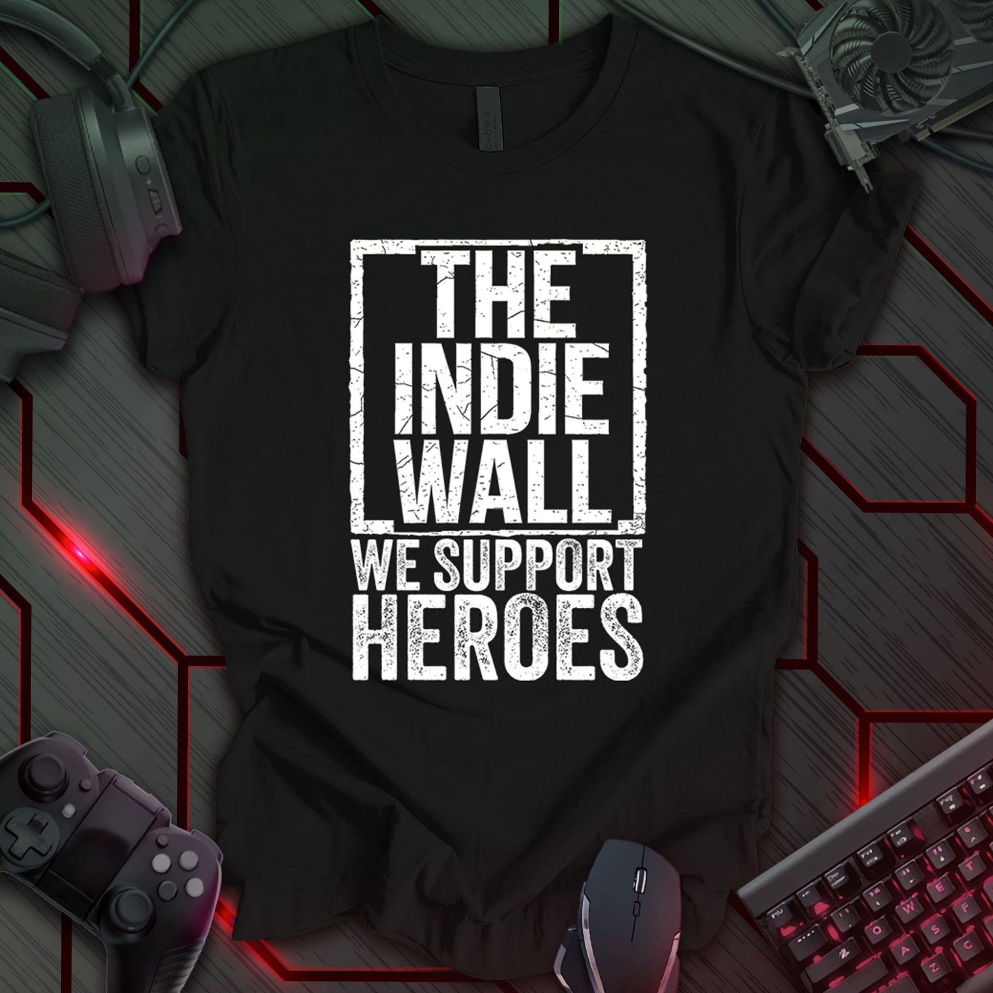 Black gaming t-shirt featuring a distressed black and white design of The Indie Wall logo. Below the logo, bold distressed text reads "WE SUPPORT HEROES," emphasizing support for indie developers and gamers.