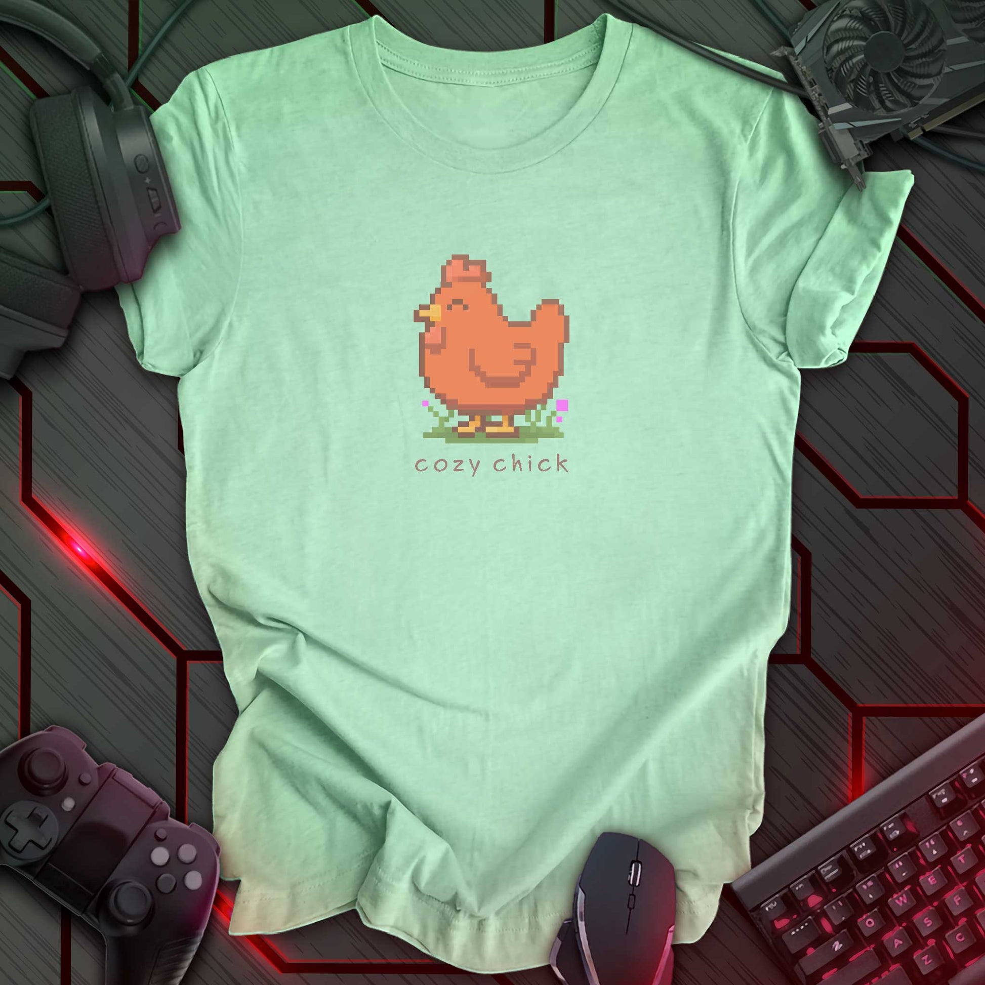 light green color t-shirt with a chest print of a pixel art image of a cute brown chick standing on a patch of grass. text beneath the pixel art reads "cozy chick".