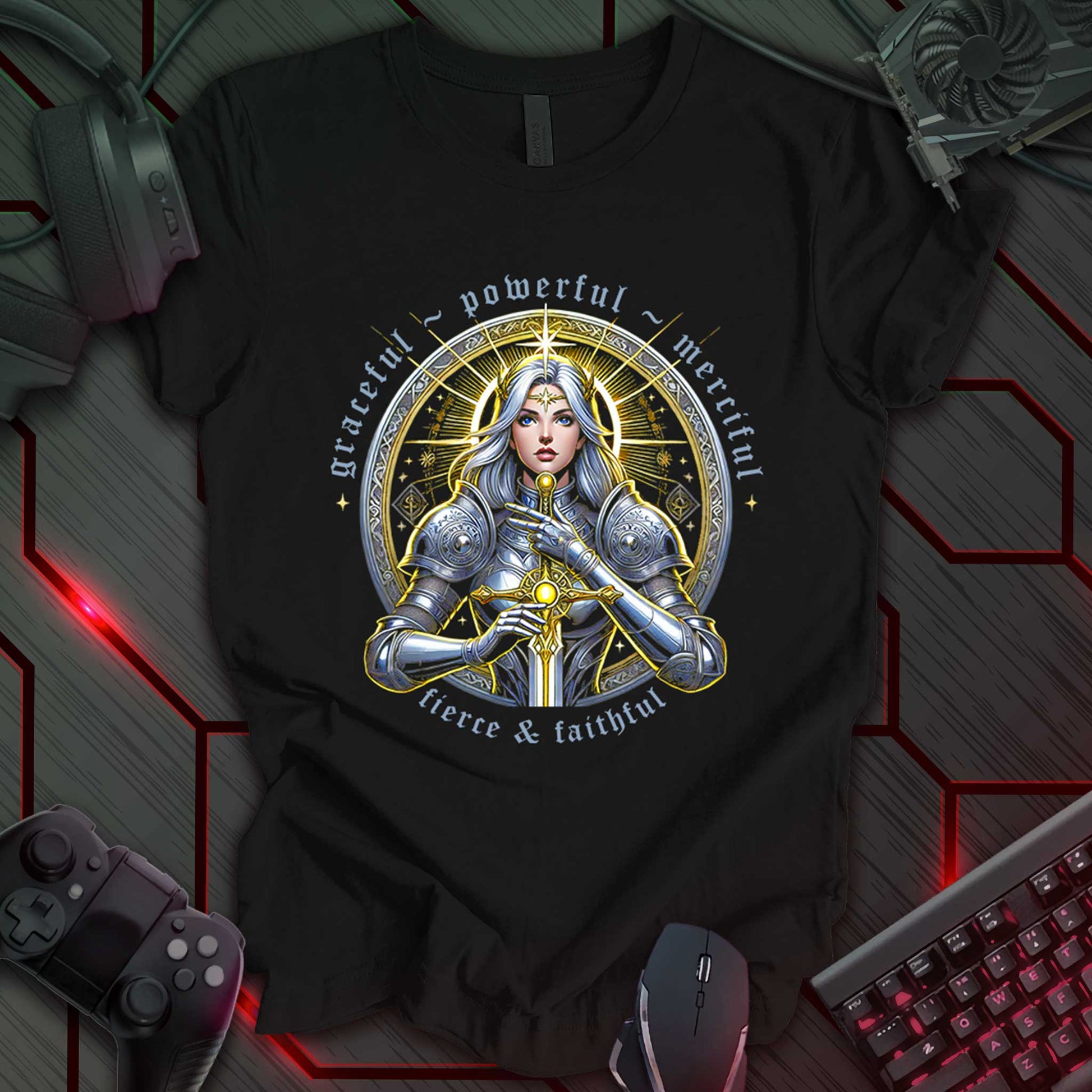 This t-shirt design, created for fans of fantasy art and strong female characters, features a detailed illustration of a female warrior in silver armor, holding a sword, against a circular, ornate golden background. The words 'graceful ~ powerful', 'merciful', and 'fierce & faithful' are arranged around the circle, with 'THE INDIE WALL' in the bottom right corner. This design appeals to those who appreciate powerful imagery and fantasy themes.