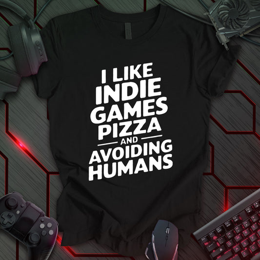 Graphic design featuring the phrase 'I LIKE' in a bold, slightly distressed font at the top, followed by 'INDIE GAMES', 'PIZZA', and 'AND AVOIDING HUMANS' each on separate lines in the same bold, distressed font. The word 'AND' is flanked by two thin horizontal lines. All text is white against a black background. This is a humorous design with an indie gaming and food theme, featuring a relatable sentiment for introverted gamers.