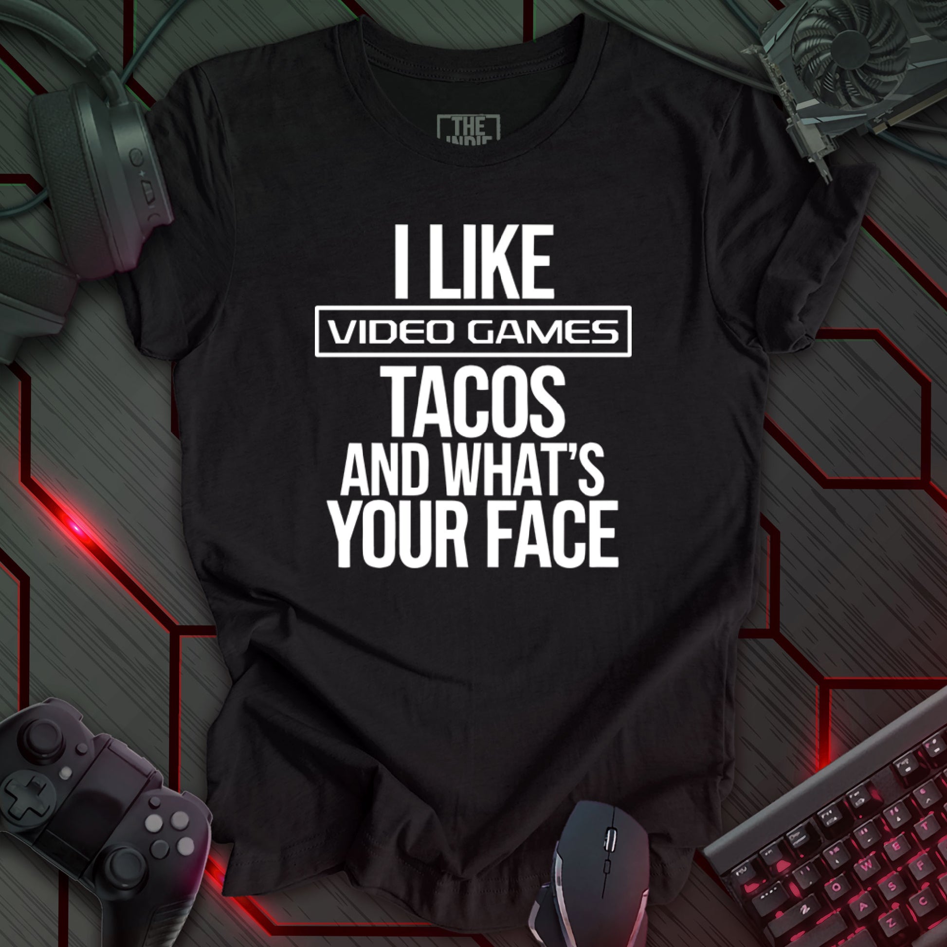 Graphic design featuring the phrase 'I LIKE' in a bold, slightly distressed font at the top, followed by 'VIDEO GAMES' with a rectangle boarder, 'TACOS', and 'AND WHAT'S YOUR FACE' each on separate lines in the same bold, distressed font. All text is white against a heather black background. This is a humorous design with an indie gaming and food theme, featuring a playful and quirky sentiment.
