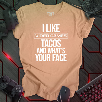 Graphic design featuring the phrase 'I LIKE' in a bold, slightly distressed font at the top, followed by 'VIDEO GAMES' with a rectangle boarder, 'TACOS', and 'AND WHAT'S YOUR FACE' each on separate lines in the same bold, distressed font. All text is white against a heather peach background. This is a humorous design with an indie gaming and food theme, featuring a playful and quirky sentiment.
