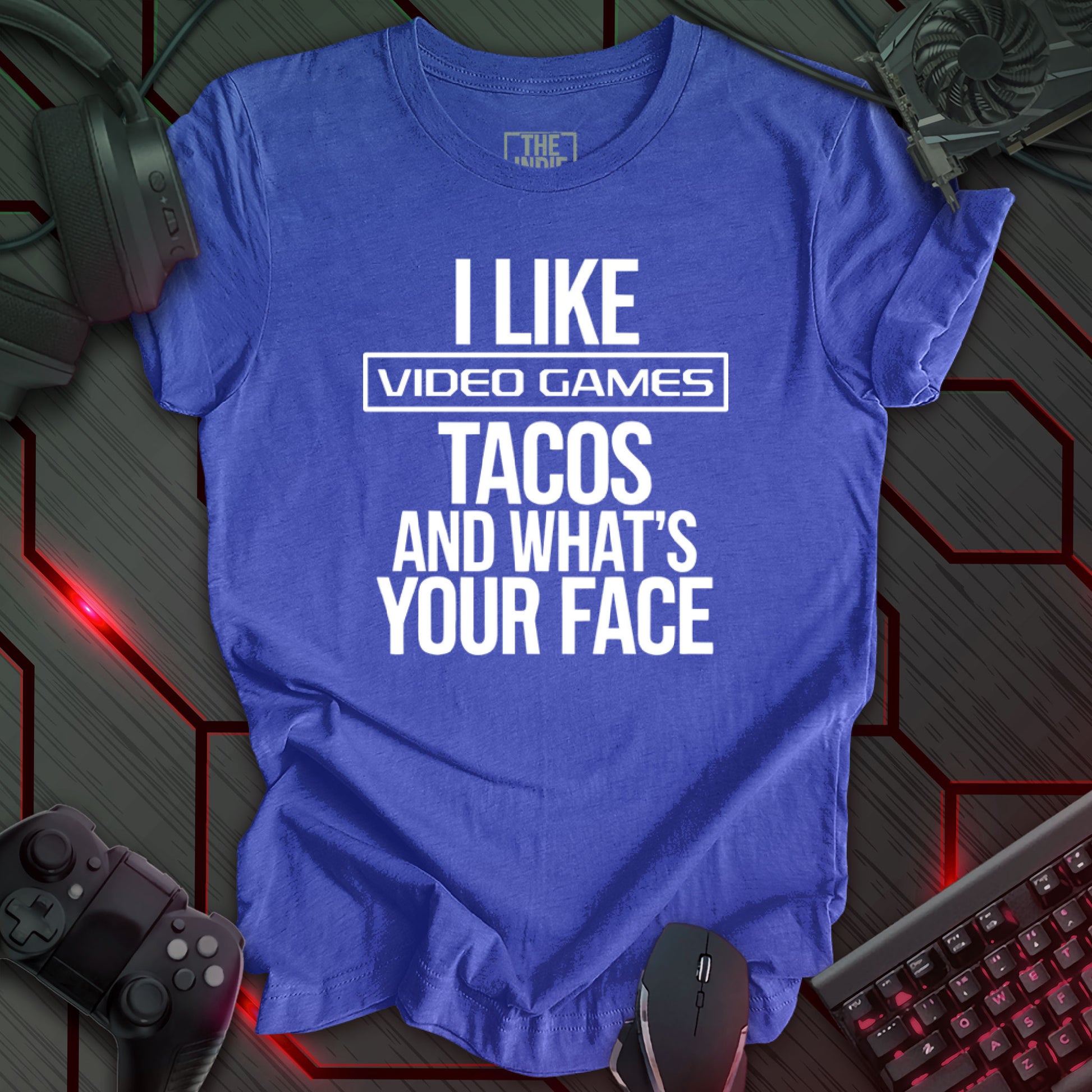 Graphic design featuring the phrase 'I LIKE' in a bold, slightly distressed font at the top, followed by 'VIDEO GAMES' with a rectangle boarder, 'TACOS', and 'AND WHAT'S YOUR FACE' each on separate lines in the same bold, distressed font. All text is white against a heather true royal background. This is a humorous design with an indie gaming and food theme, featuring a playful and quirky sentiment.
