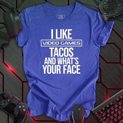 Graphic design featuring the phrase 'I LIKE' in a bold, slightly distressed font at the top, followed by 'VIDEO GAMES' with a rectangle boarder, 'TACOS', and 'AND WHAT'S YOUR FACE' each on separate lines in the same bold, distressed font. All text is white against a heather true royal background. This is a humorous design with an indie gaming and food theme, featuring a playful and quirky sentiment.
