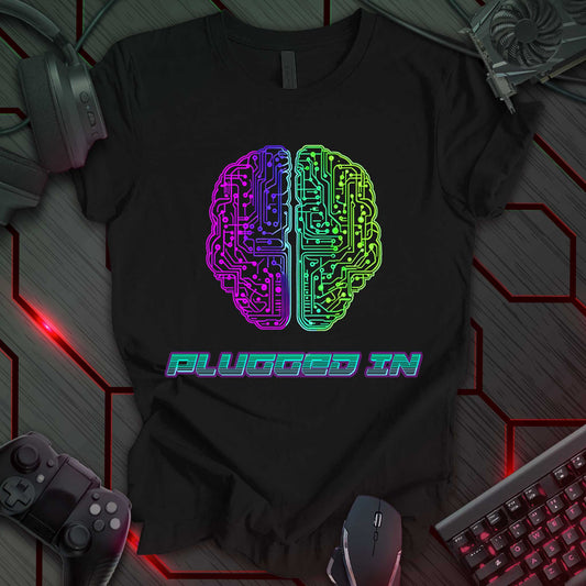 Digital illustration of a stylized brain, split vertically into two halves. The left half is rendered in shades of purple and blue, while the right half is rendered in shades of green and yellow, both featuring circuit board patterns. The brain is centered against a black background. Below the brain is the phrase 'PLUGGED IN' in a blocky, outlined font, rendered in shades of teal and purple. This is a design with a technology or cyberpunk theme, featuring a brain chip and the phrase 'PLUGGED IN'.